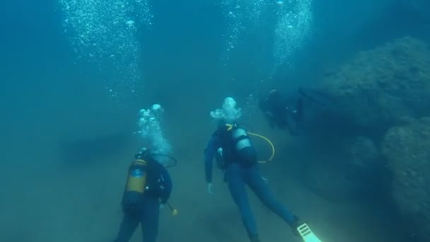 Профессиональные водолазы в желтых плавниках, плавающие вдоль морского дна, пузырьки воздуха поднимаются — стоковое видео