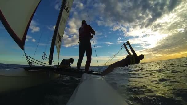 Три человека плывут на виндсерфинге на катамаране против сумеречного неба над океаном — стоковое видео