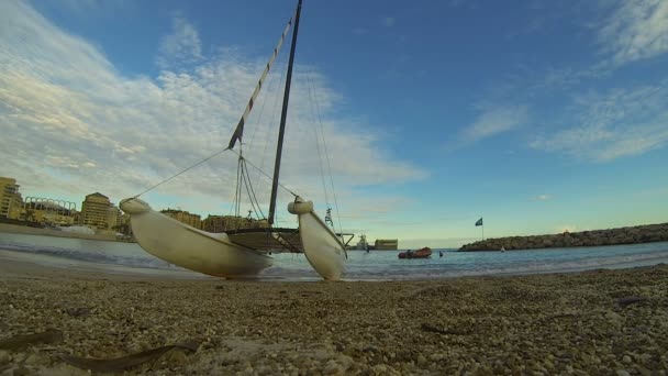 Βοτσαλωτή ακτή με καταμαράν windsurfing, λήξης ουρανός και πόλη στο πίσω μέρος, τουρισμός — Αρχείο Βίντεο