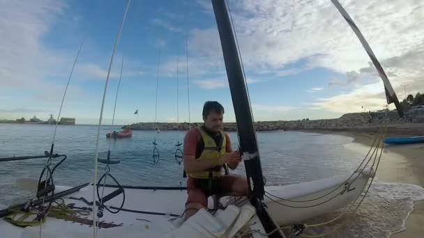 Mann auf Windsurf-Katamaran macht sich bereit zum Segeln, zieht Seile am Mast fest — Stockvideo