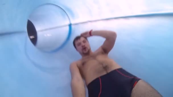 Молодой парень спускается по горке в аквапарке, снимает себя веселящимся — стоковое видео