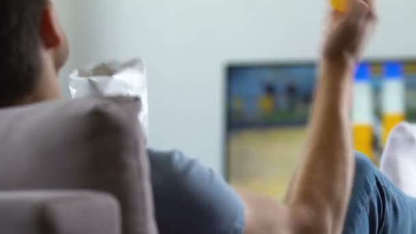 Emotional football fan watching match on TV at home, eating chips, back view — Stock Video