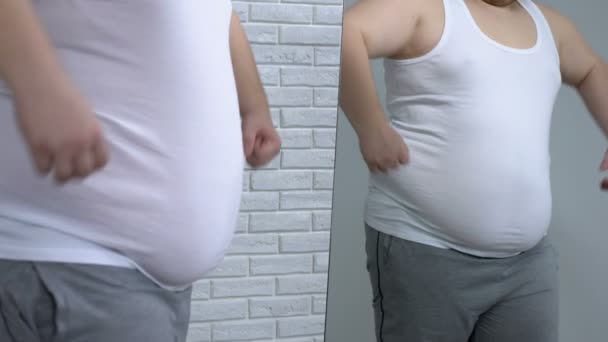 Tlustý mladík pózuje v zrcadle, předstírá, že svalnatý, fitness a dieta — Stock video