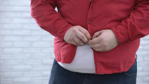 Толстяк застегивает красную рубашку и тянет вниз, проблема с огромной тканью — стоковое видео
