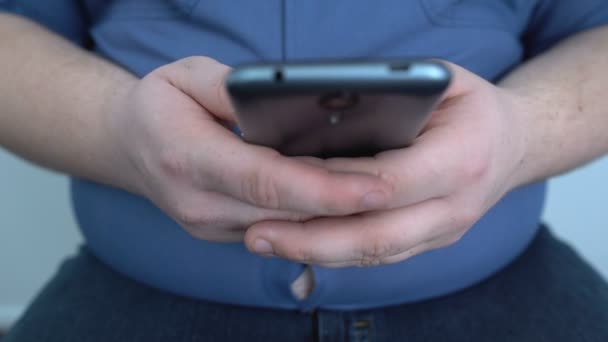Ленивый толстяк, играющий в игры на смартфоне, общающийся с друзьями, сидячий образ жизни — стоковое видео