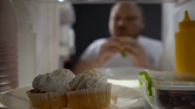 Şişman adam hamburger buzdolabı, abur cubur bağımlılığı, obezite önünde çiğneme