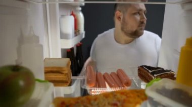Bağımlısı genç adam yeme sosis buzdolabı, sağlıksız beslenme yakınındaki geceleri