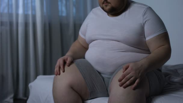 Fat Man masseren knieën zittend op bed, gewrichtsontsteking, orthopedische aandoening — Stockvideo