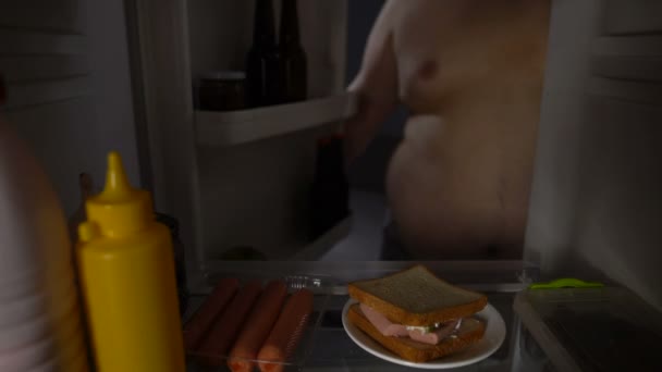 Толстый мужчина берет сэндвич из холодильника, нездоровое питание, сидячий образ жизни — стоковое видео