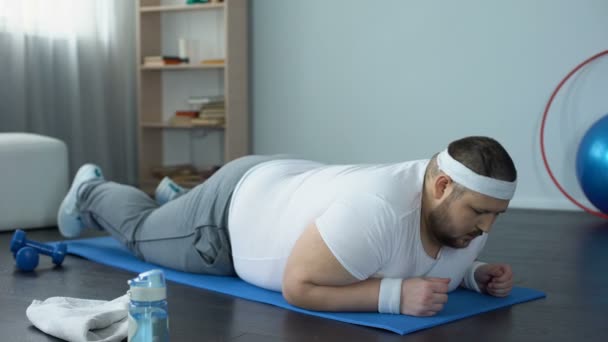 Målmedveten överviktig man gör plankan övning på hem, önskan att gå ner i vikt — Stockvideo