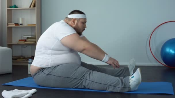 Trött överviktig man stretching och faller ner mattan efter ansträngande träning — Stockvideo