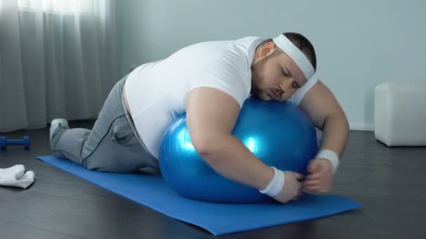 Слабко-вольовий товстий чоловік, що розслабляється на фітнес-кулі, домашня перерва тренування, лінь — стокове відео