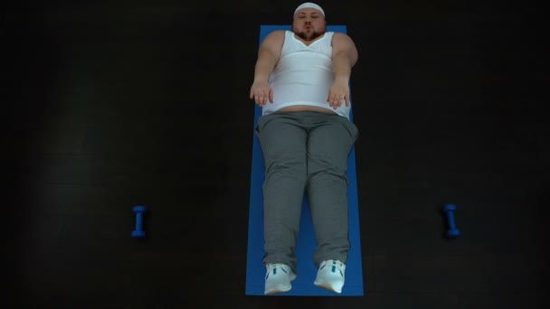 Толстый молодой мужчина укрепляет мышцы брюшной полости, сжигает жир в животе, спорт — стоковое видео