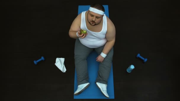 Homem gordo faminto comendo maçã verde após o treino de ginástica, nutrição saudável, vista superior — Vídeo de Stock