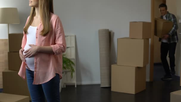 Fille enceinte regardant nouvel appartement tandis que son mari portant des boîtes, crédit — Video