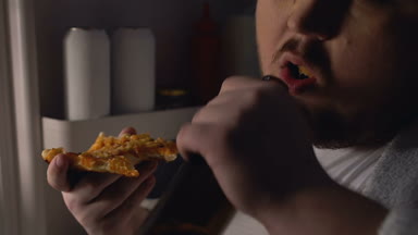 Pizza yeme ve içme bira ayakta buzdolabı yakınındaki zayıf iradeli kilolu adam