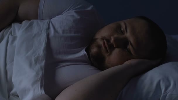 Надмірна вага чоловік спить в ліжку вночі, відпочиває на зручній подушці, мріє — стокове відео
