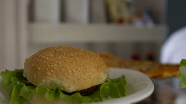 Hungriger Mann nimmt Hamburger aus Kühlschrank und kaut, Diätfehler, Junk Food — Stockvideo
