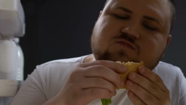 デブの男が熱心に夜、心理的食品依存性、中毒でハンバーガーを食べる — ストック動画