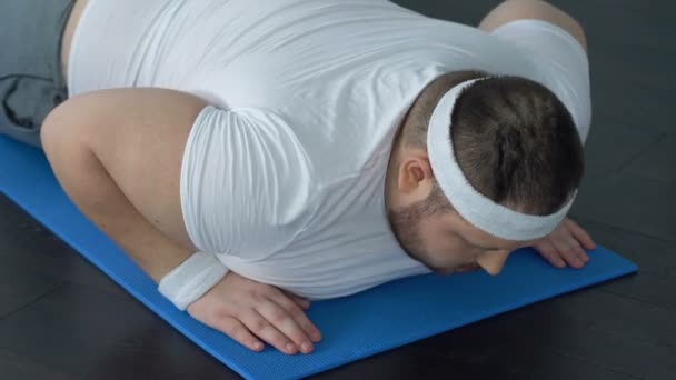Товстий чоловік падає на йога килимок намагається робити дошку вправи, відсутність енергії — стокове відео