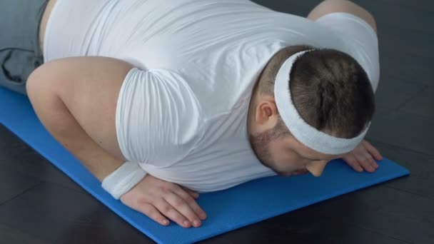 Hombre gordo cayendo en la esterilla de yoga tratando de hacer ejercicio de tablón, falta de energía — Vídeos de Stock