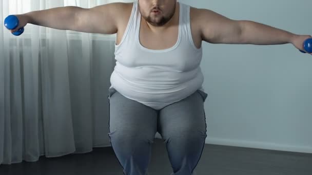 Мотивований товстий чоловік здійснює присідання і піднімає гантелі зміцнюючи м'язи — стокове відео