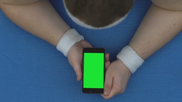 Sportsman watching online fitness video, lying smartphone on mat, workout break — Stock Video