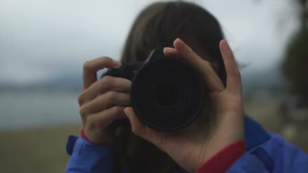 Женщина-репортер фотографирует на пляже в холодную погоду, объектив камеры крупным планом — стоковое видео