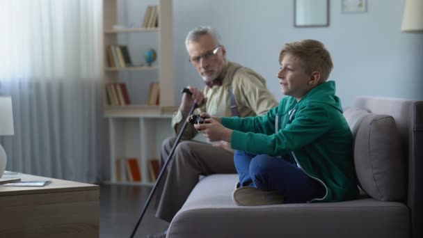 Незадоволений дідусь дивиться на щасливого онука, який грає в розрив генерації відеоігор — стокове відео