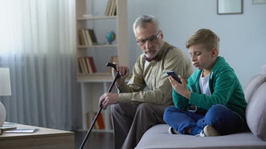 Çocuk kaydırma blog sayfalarında smartphone, dedesi terk edilmiş hissediyor, üzgün