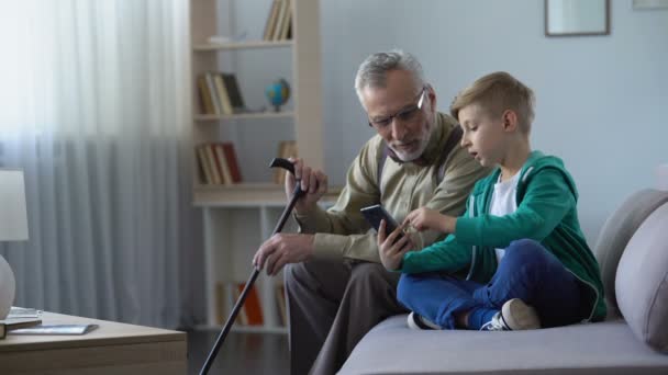 Chico explicando al abuelo cómo usar el teléfono celular, tecnologías simples para el anciano — Vídeos de Stock