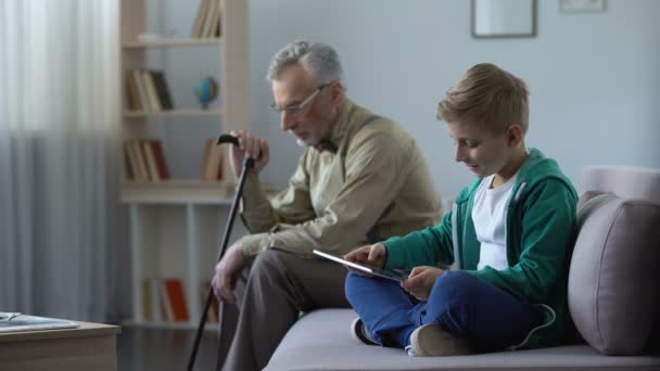 Jongen afspelen van video game op tablet, geen aandacht op eenzame opa — Stockvideo