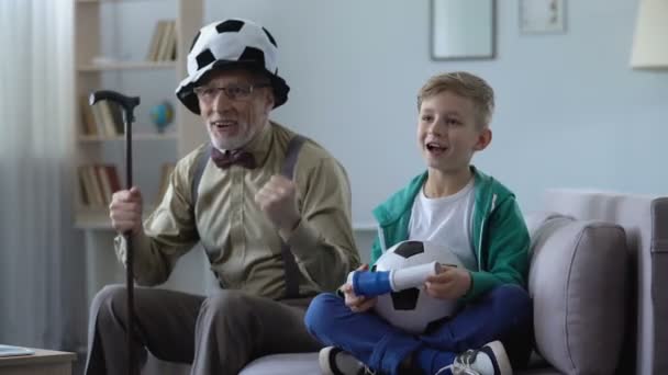 Grandpa in crazy football hat and boy cheering for national team with fan horn — Stock Video