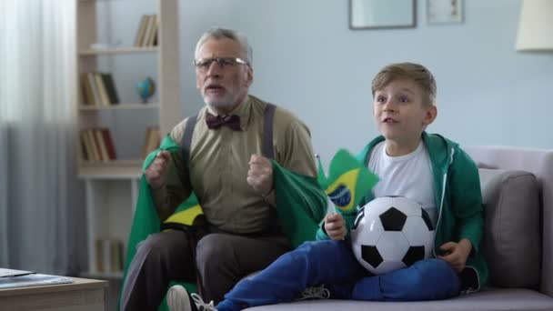 Avô agitando bandeiras do Brasil junto com neto, assistindo futebol em casa — Vídeo de Stock