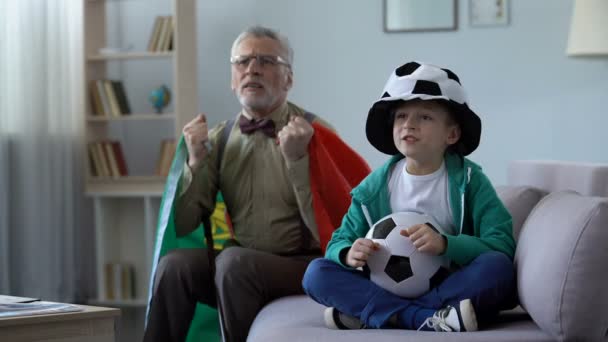 Старий португальський розмахував прапором, дивитися футбол разом з онуком вдома — стокове відео