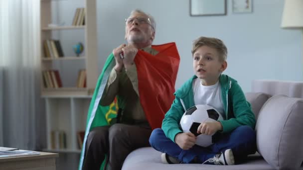Grandpa and grandson watching football, waving Portuguese flag, happy for win — Stock Video
