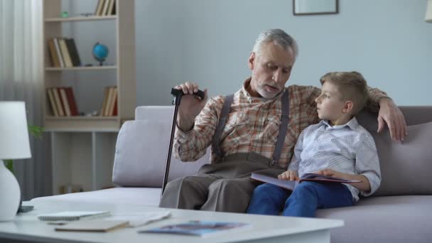 Grandpa watching photo album with grandson, remembering youth, telling stories — Stock Video