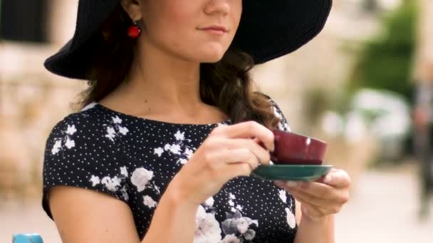 Mujer inteligente en sombrero bebiendo café en la cafetería de la calle, disfrutando de vacaciones — Vídeo de stock