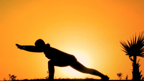Силует гнучкої жінки, що практикує йогу на вершині гори на заході сонця, спорт — стокове відео