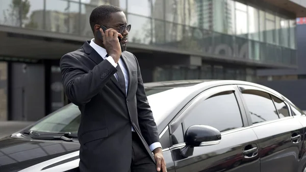 Successful man in expensive suit communicating on phone, standing near his car