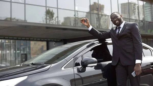 Pleased African American man showing key from new luxury car, dreams come true