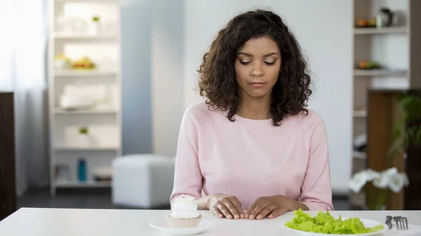 Young beautiful woman making choice of cake and salad, will power, weight loss