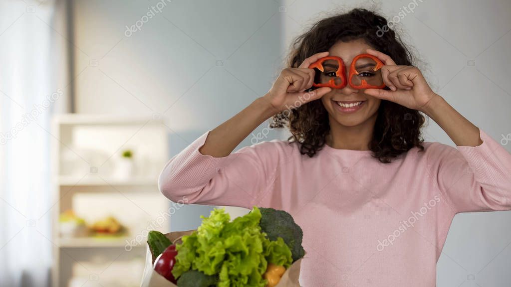 Beautiful woman holding pepper rings near eyes smiling, healthy eating habits