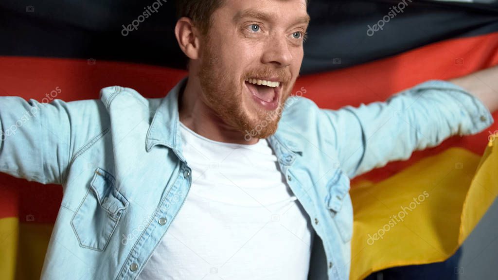 German supporter holding national flag, watching football match, rejoicing goal