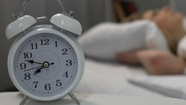 Reloj despertador sonando y despertando mujer rubia acostada en la cama, hora de la mañana — Vídeo de stock