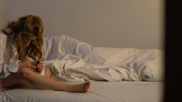 Ревнивая жена сидит в постели и просматривает сообщения в отношениях мужа смартфона — стоковое видео