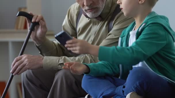 Пожилой мужчина и внук смотрят видео на смартфоне вместе, семейная близость — стоковое видео