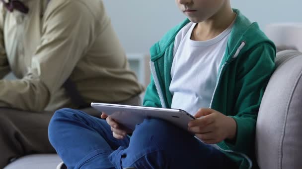 Jongen lezen boek op tablet zittend op de Bank met grootvader, jonge generatie — Stockvideo