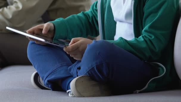 Hijo jugando tableta juego sentado con el padre en el sofá en la sala de espera, adicción — Vídeo de stock