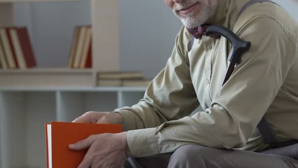 Улыбающийся пожилой мужчина читает книгу дома, мирный выход на пенсию, свободное время расслабиться — стоковое видео